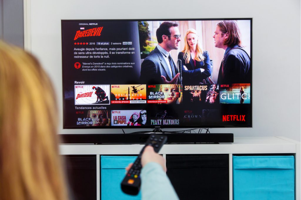 Woman Holding a TV remote control and play Dardevil, a Marvel film that is an original creation of Netflix industry.