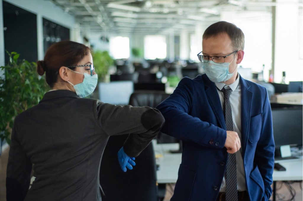 A man and a woman in medical masks maintain a social distance at work.