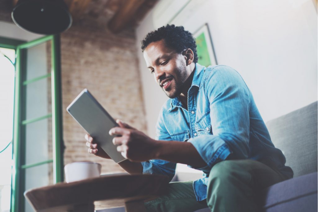 Man enjoys reading using tablet while relaxing on sofa.