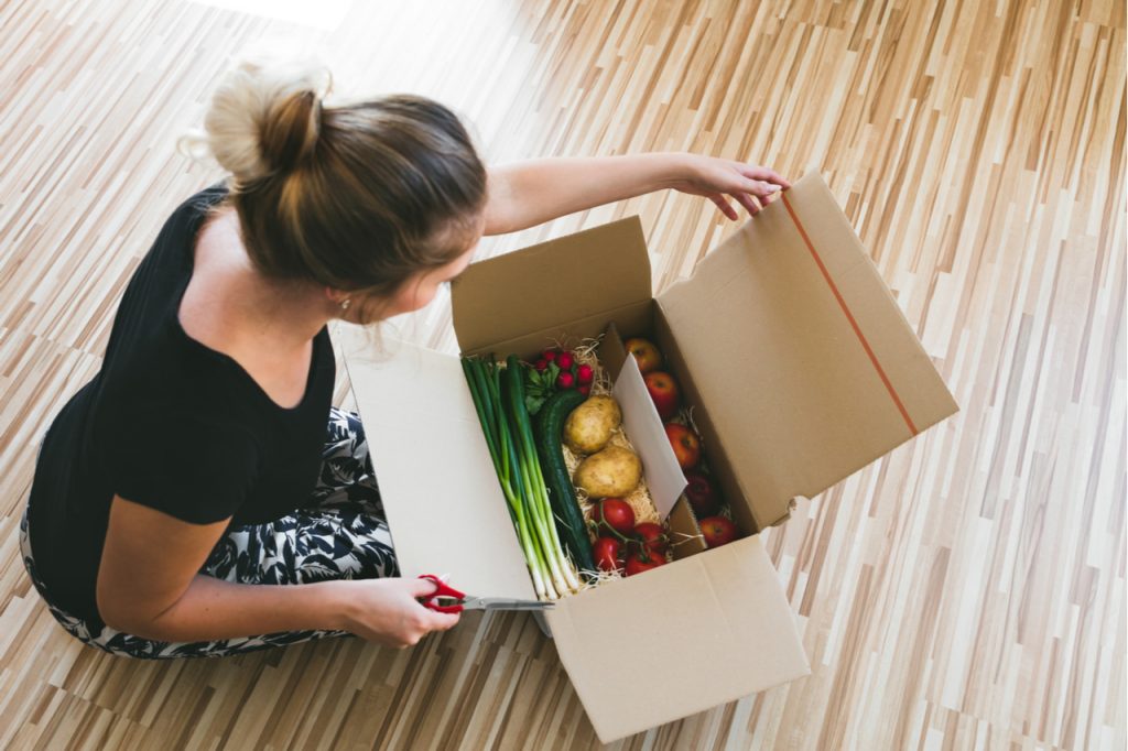 Woman opening a vegetable delivery box at home, online ordering.