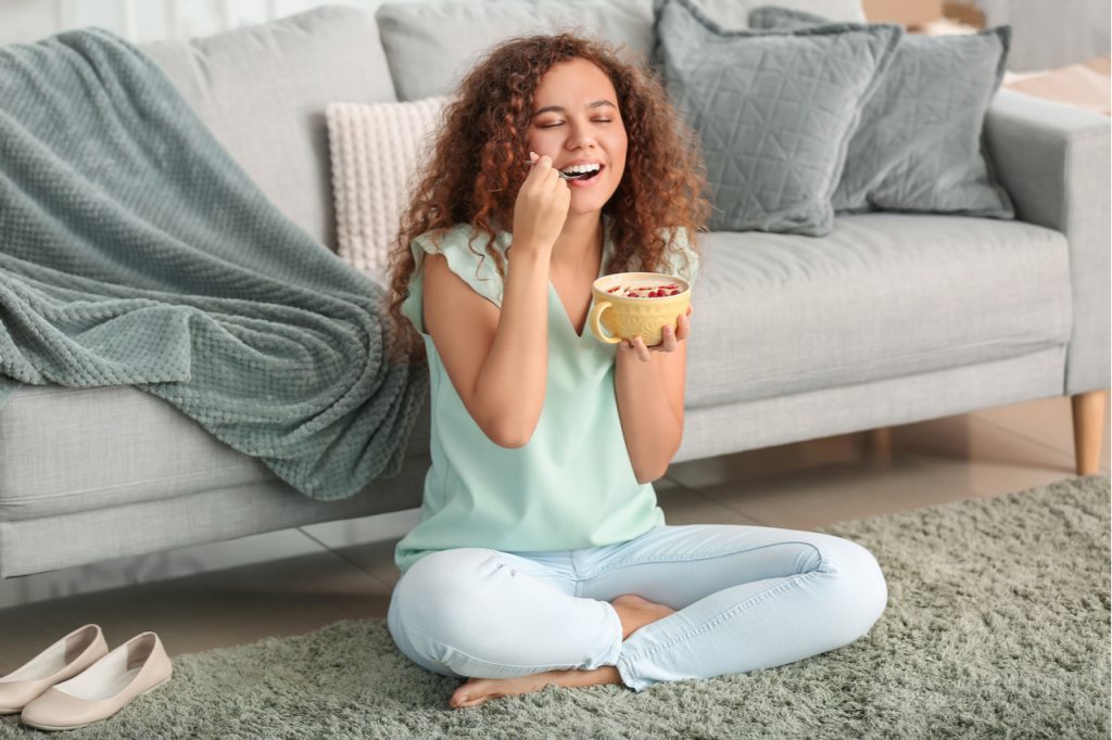 Young woman eating tasty yogurt at home.