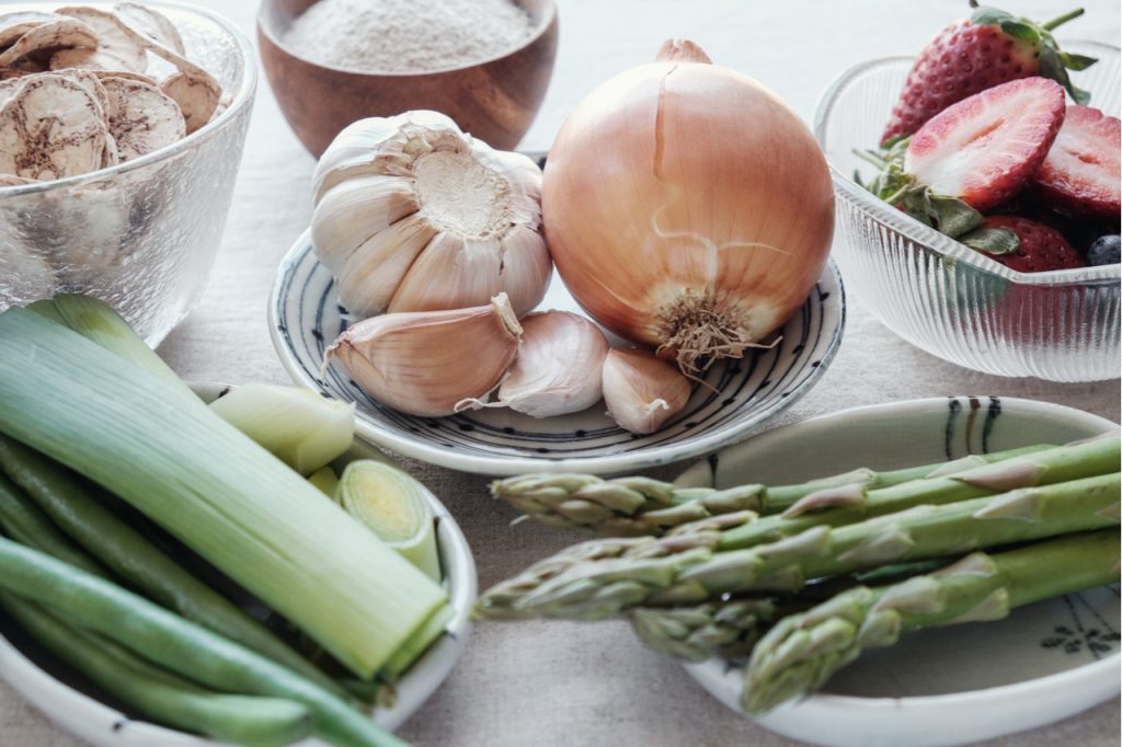 Onions, garlic cloves, leaks, asparagus, sliced strawberry and a bowl of mushroom.