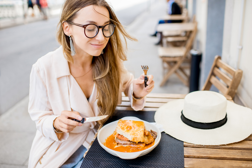 Woman eating traditional portuguese sandwich with meat called francesinha sitting at the restaurant in Porto city, Portugal