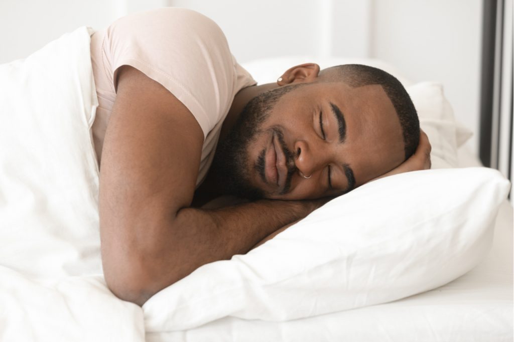 Man sleeping well alone under warm duvet feeling comfortable coping with the new normal.