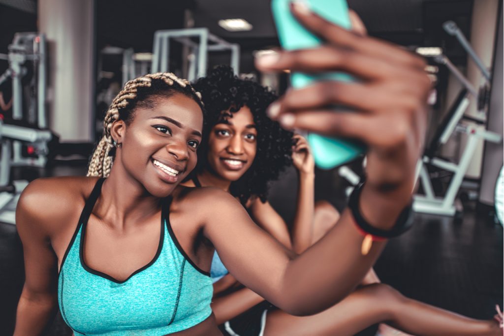Two smiling beautiful girls in the gym do selfie embracing the digital life.