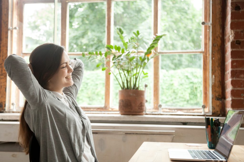 A young woman relaxing and smiling while in front of her laptop. How to handle stress for her is taking control of the situation.