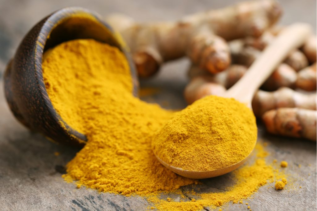 Turmeric powder and fresh turmeric on wooden background.