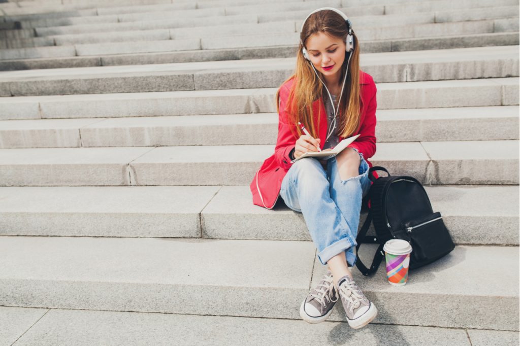 A woman writing on her journal while sitting on the steps of a stairs in the city.