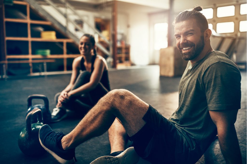 Fit people in exercise gear sitting together on the floor of a gym laughing together after a workout.