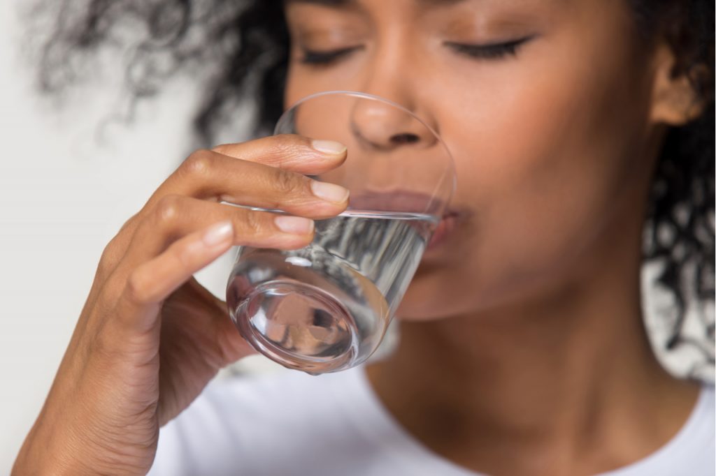 Close up focus on female drinking a glass of water in between drinking low calorie cocktail to try this labor day.
