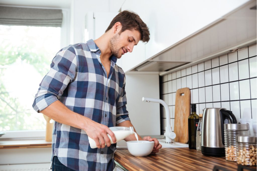 A fit man pouring milk on a bowl.