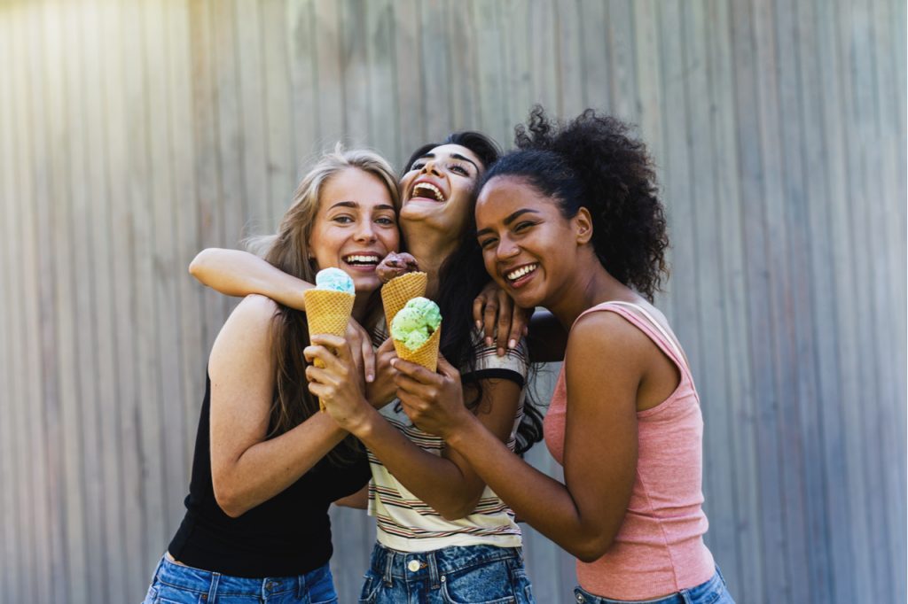 Three laughing girl friends with halo top creamery sea salt caramel standing outdoors together.