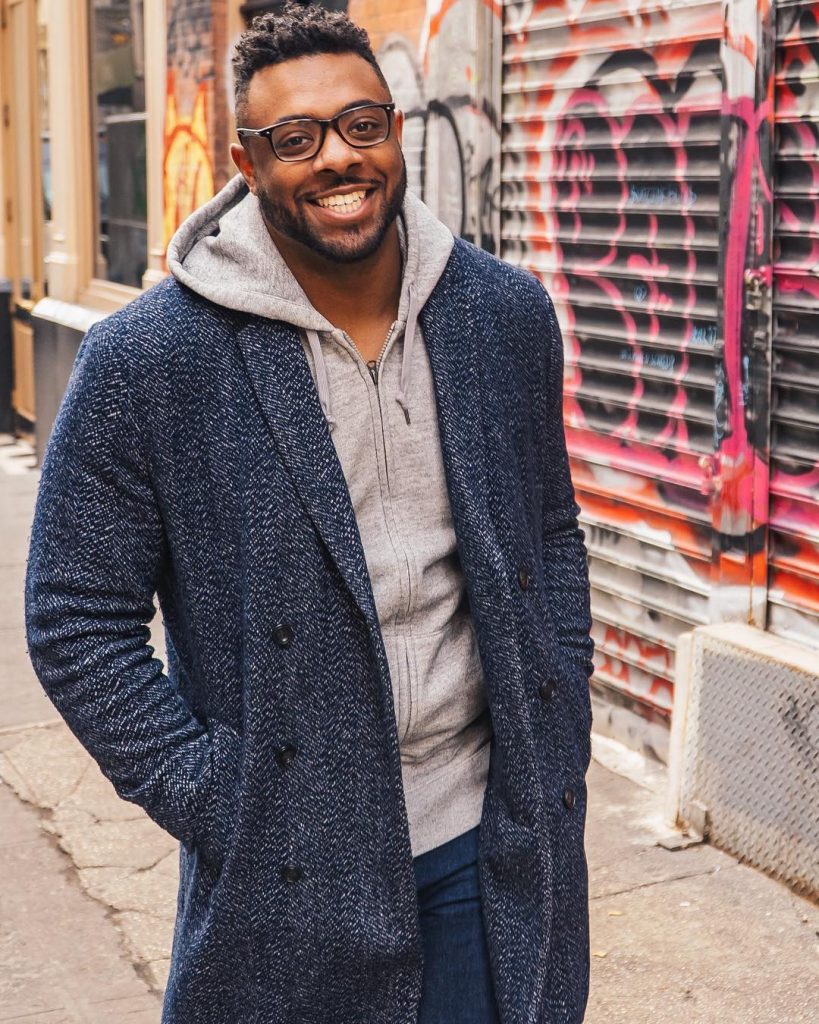A photo of Eric Dunn wearing an overcoat and a gray hoodie with a smile on his face.