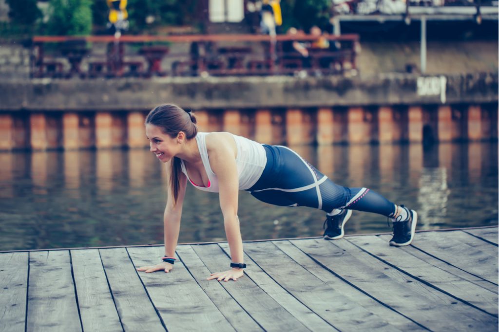 Determined young woman doing push up in nature, by the river.