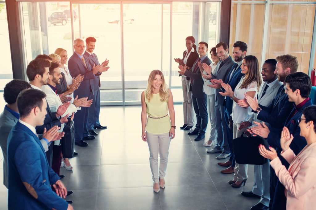 Female leader smiling as she walks in to her company building while receiving applause.