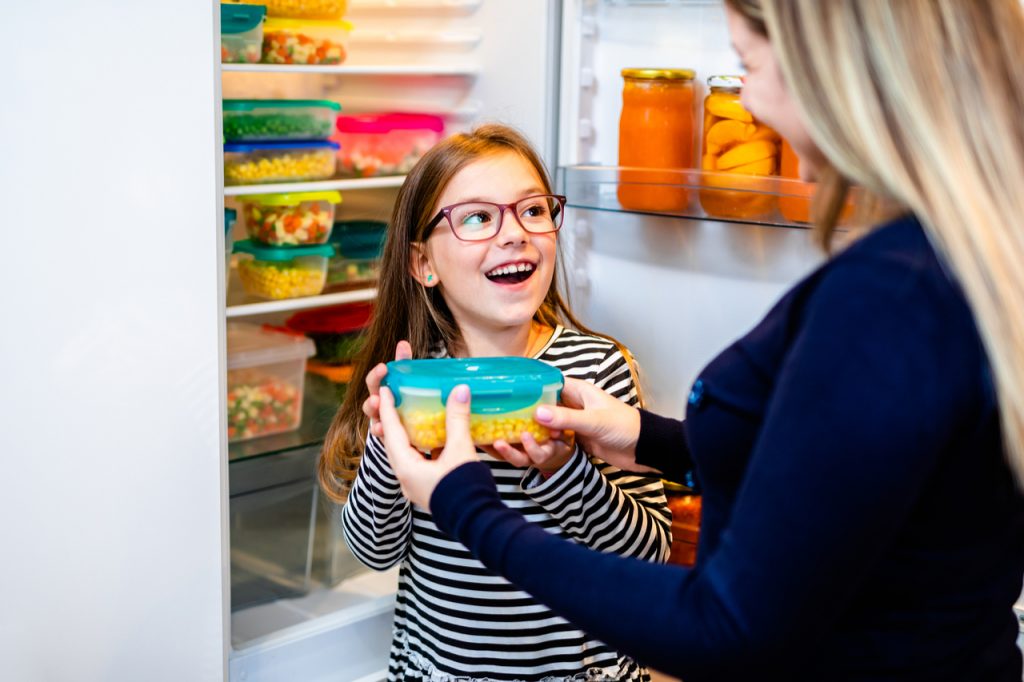 Mother and daughter putting a container of vegetables in the freezer. They always have fresh foods in their freezer.