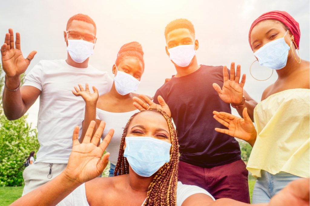 Group of five friends female and male in medical mask taking selfie on camera smartphone and having fun outdoors.