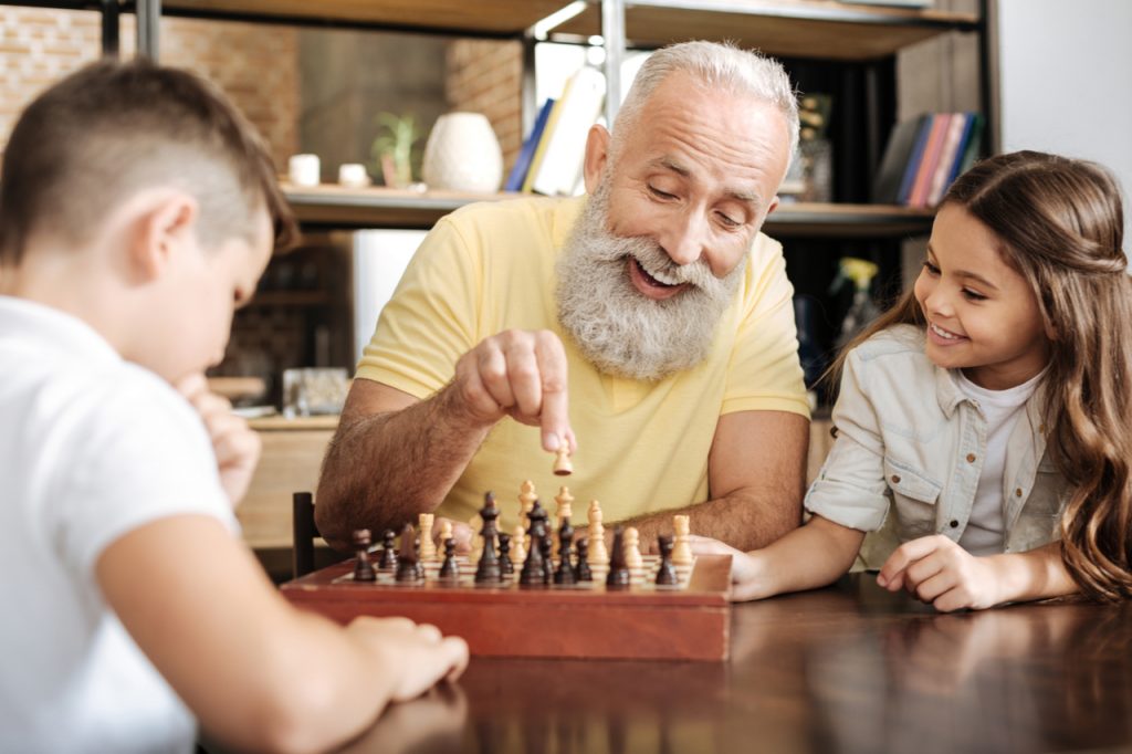 Little girl watching her brother and grandfather play chess.
