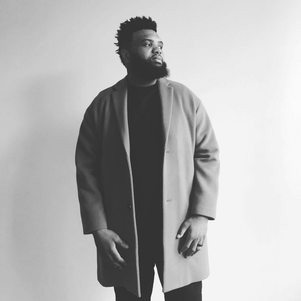 A black and white or grayscale shot of Jeff Allen wearing a coat and black shirt