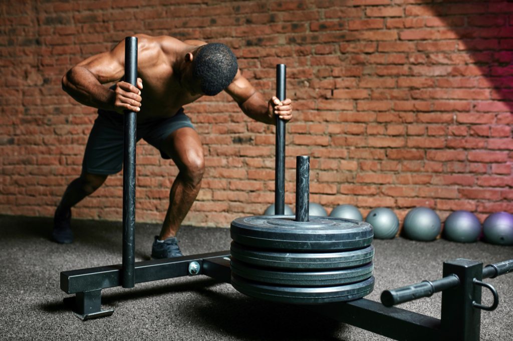 Sportsman pushing sled in cross training gym.
