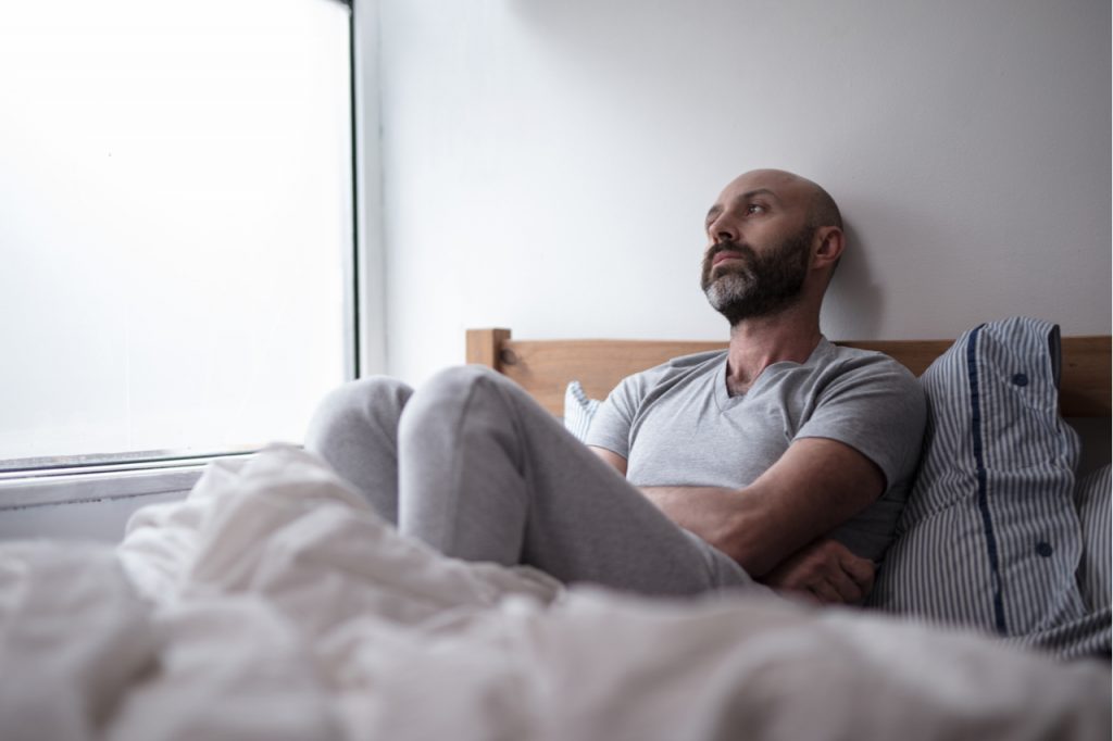 A lonely looking man on his bed staring off in space.