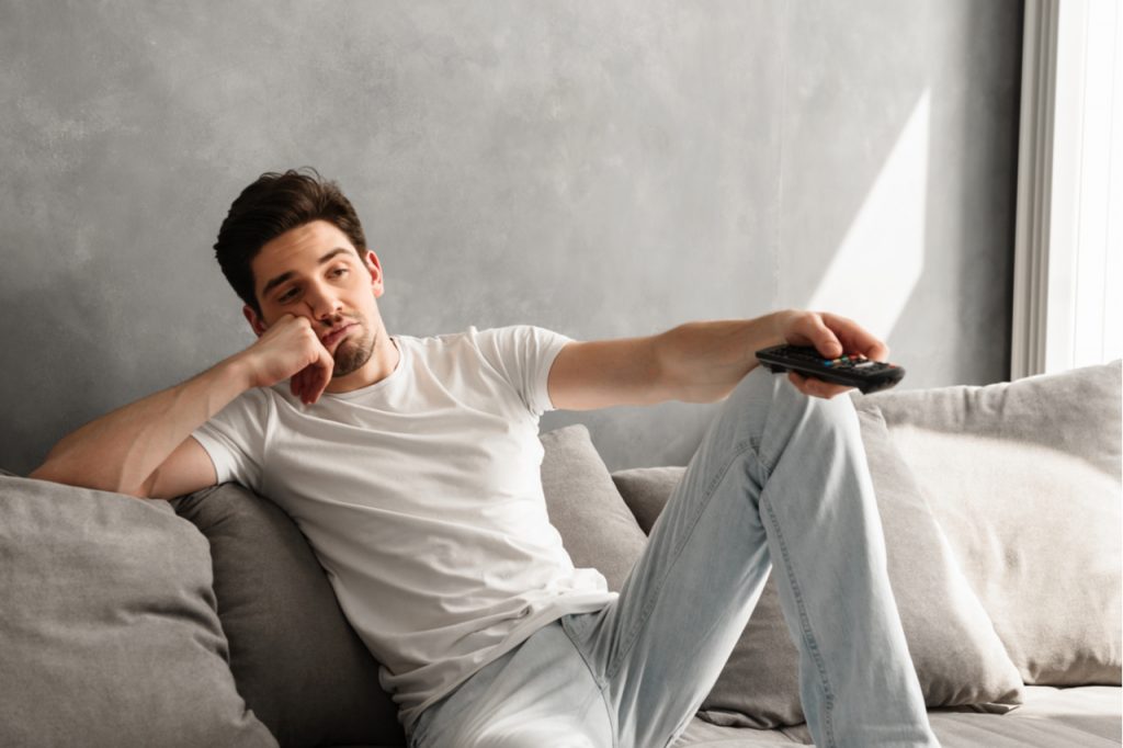 A man sitting on the couch looking bored while watching TV at home.