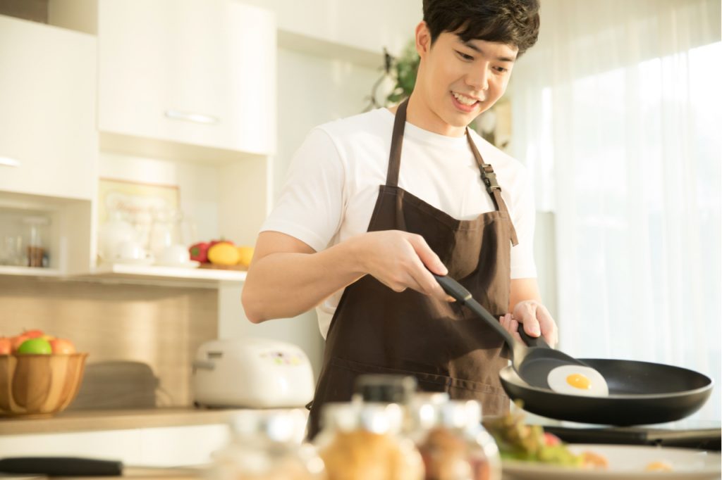 An Asian man cooking sunny side up egg.