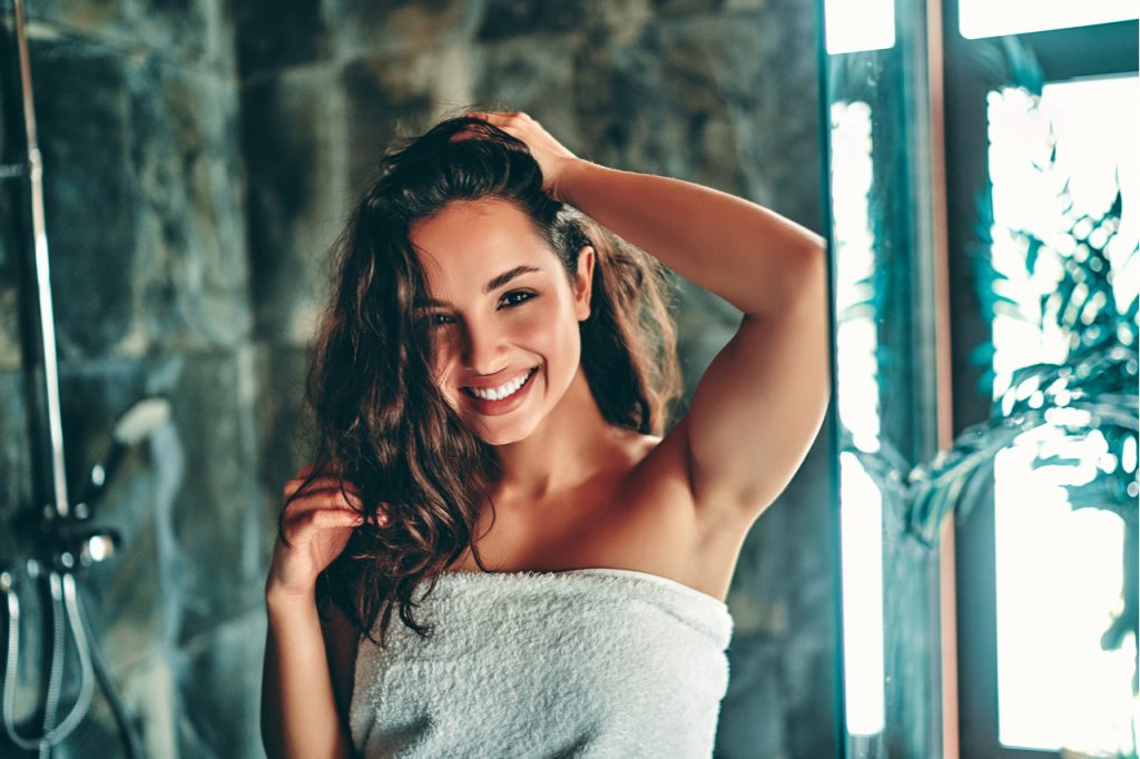 Woman taking shower in light modern light bathroom.