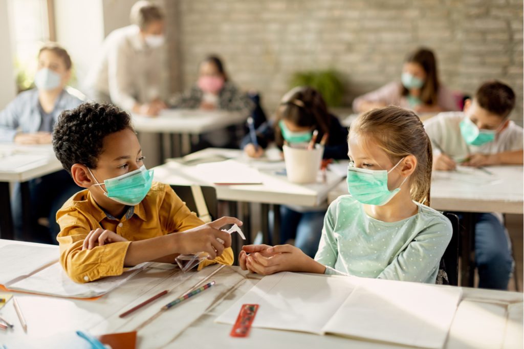 Spraying classmate's hands with disinfectant while wearing protective face masks for back to school.