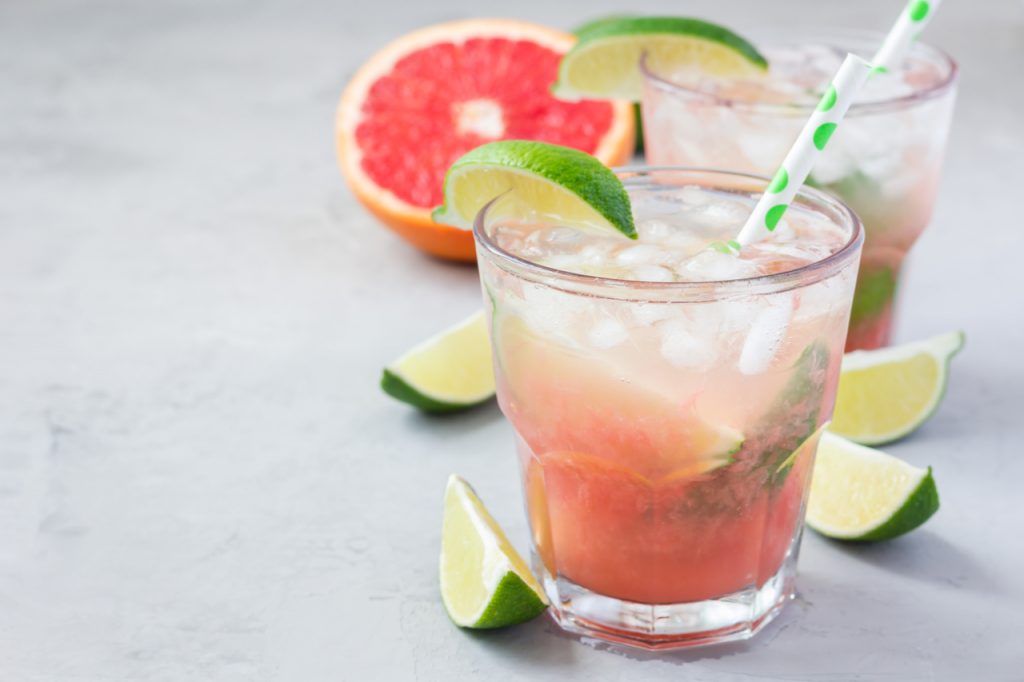 Paloma cocktail with fresh grapefruit, lime and ice cubes on concrete background.