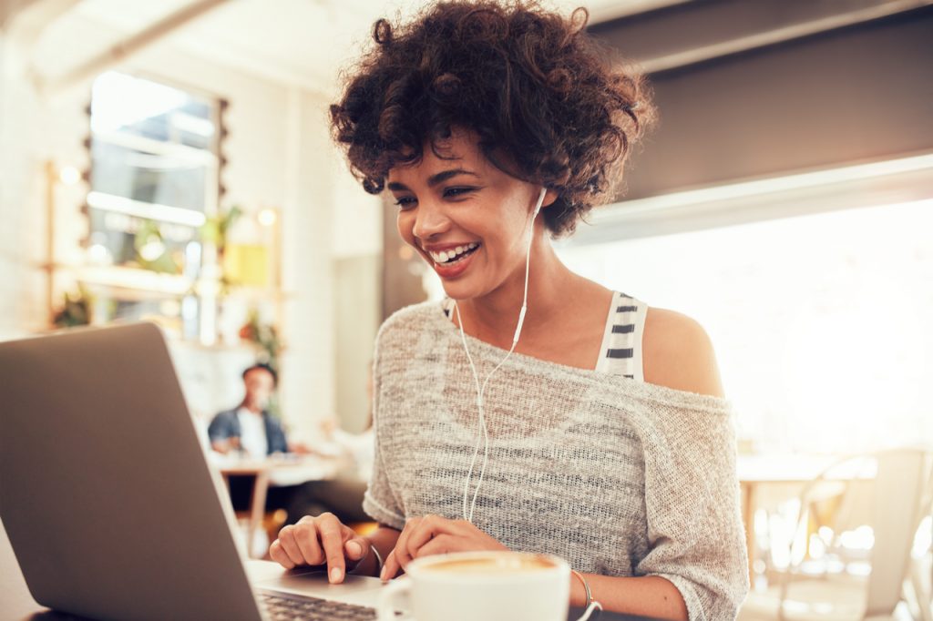 Image of happy woman using laptop while sitting at cafe.