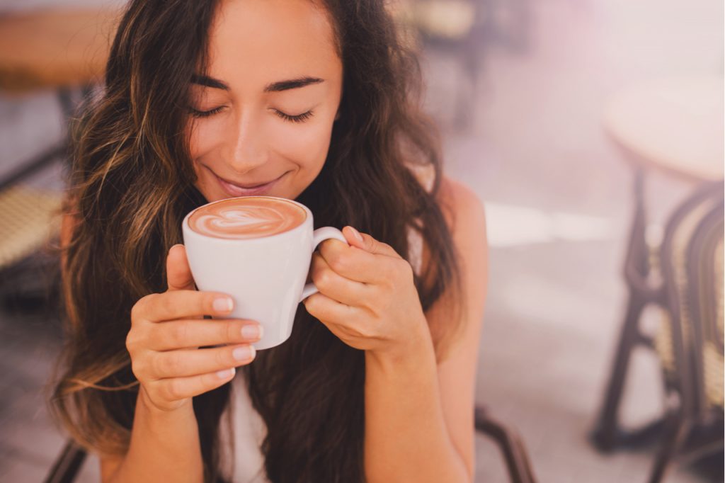 Woman with long curly hair enjoying cappuccino in a street cafe.