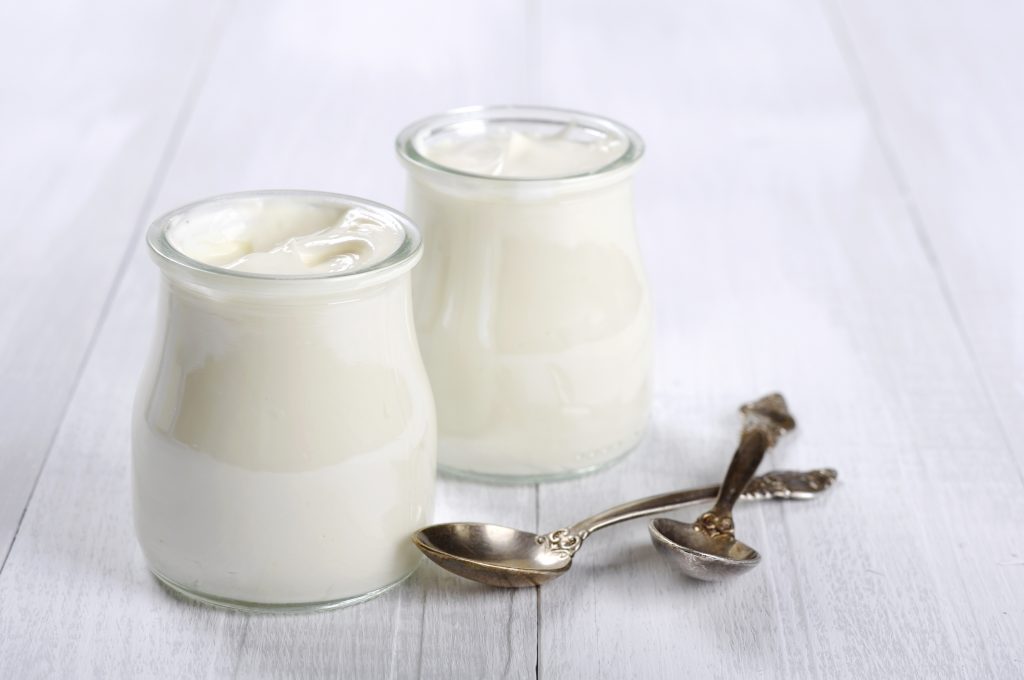 Greek yogurt in a glass jars with spoons on wooden background