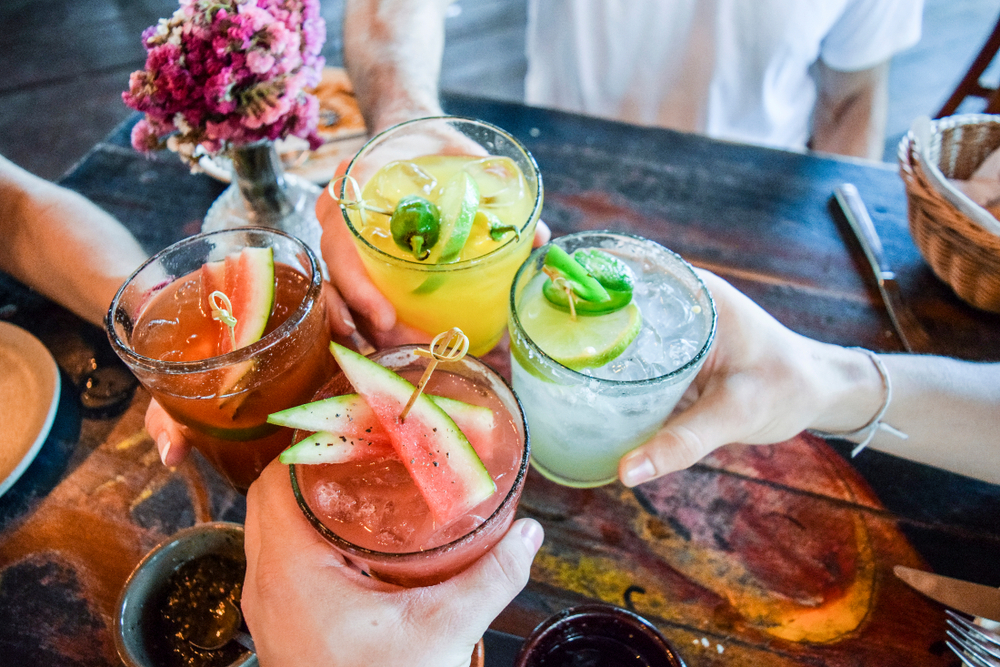 Friends toasting, saying cheers holding tropical blended fruit margaritas. Watermelon and passionfruit drinks.