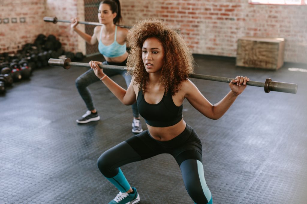 Young women exercising with barbell in fitness class.