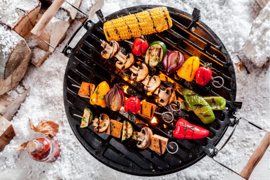 Overhead view of colorful vegetable kebabs and a corncob grilling on a BBQ outdoors for barbecue recipes.