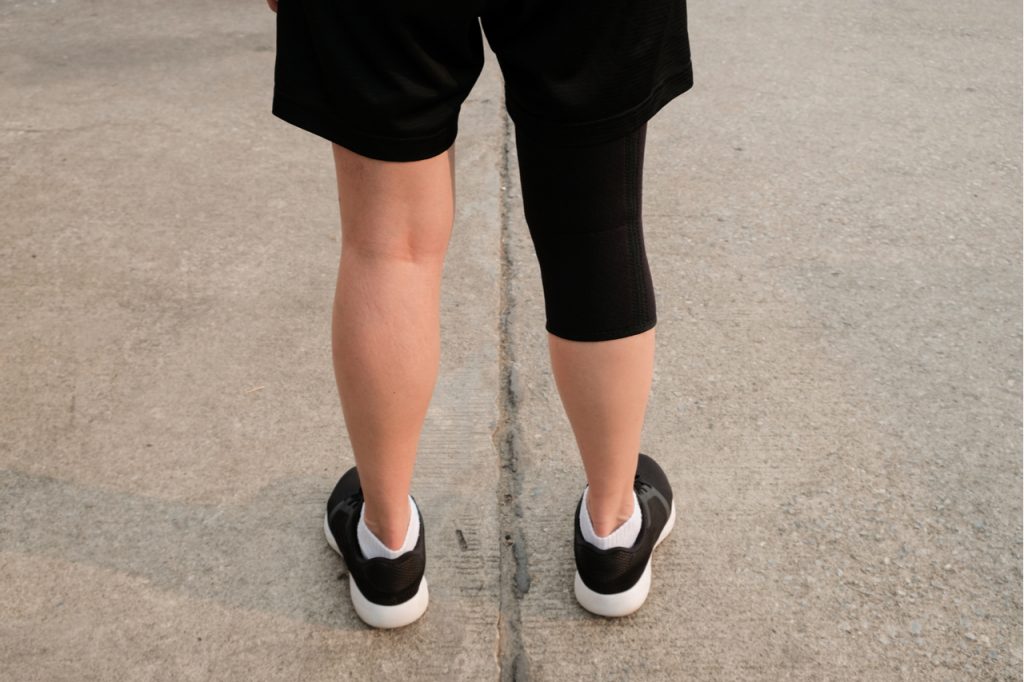Back side of runner woman wearing knee support to prevent and reduce knee pain from running.