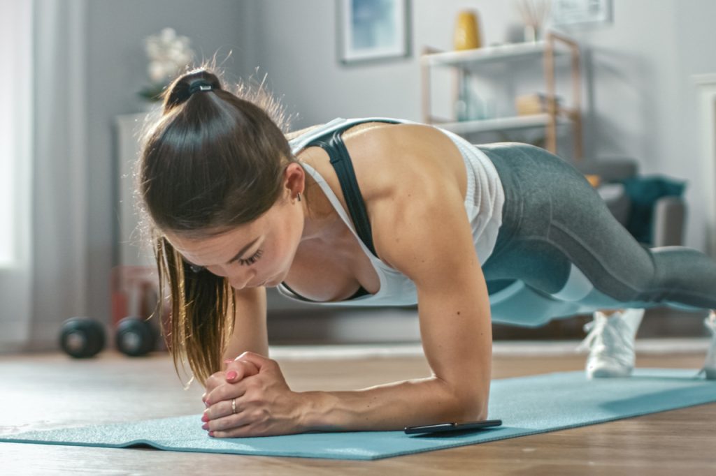 A fit woman doing plank workout at home trying to do the deck of pain workout.