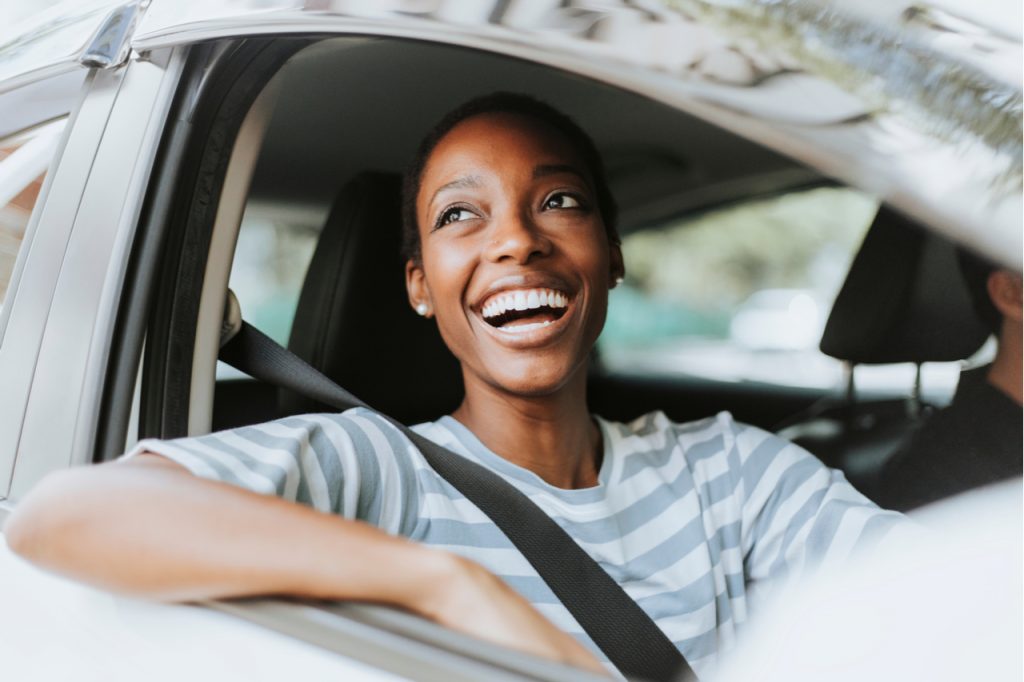 A woman looking happy while traveling by car. Seems like her trip is going smoothly without heavy traffic.
