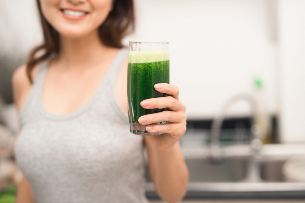 Smiling woman holding a glass of green drink.
