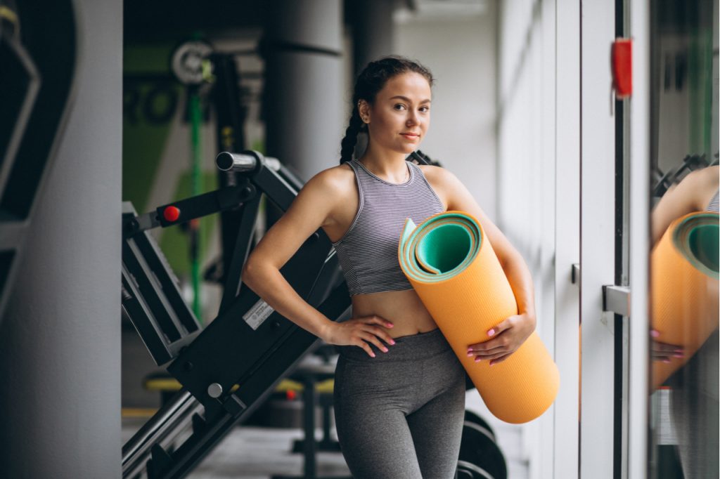 A woman bringing her own yoga mat in the gym for her own health and safety. 