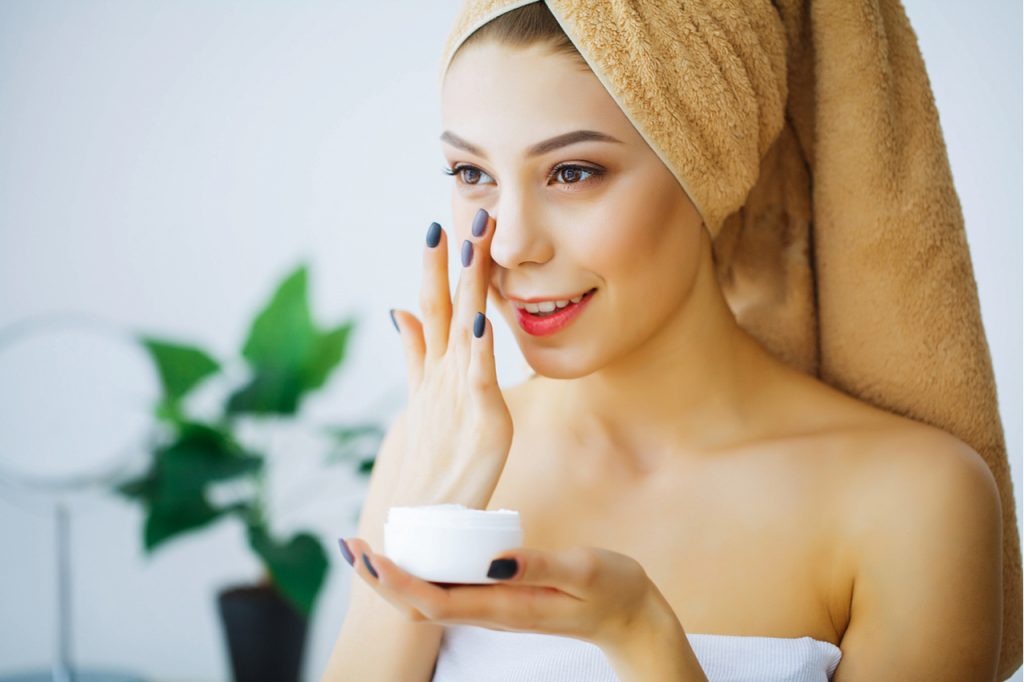 A woman applying sunscreen to her face after taking a bath.
