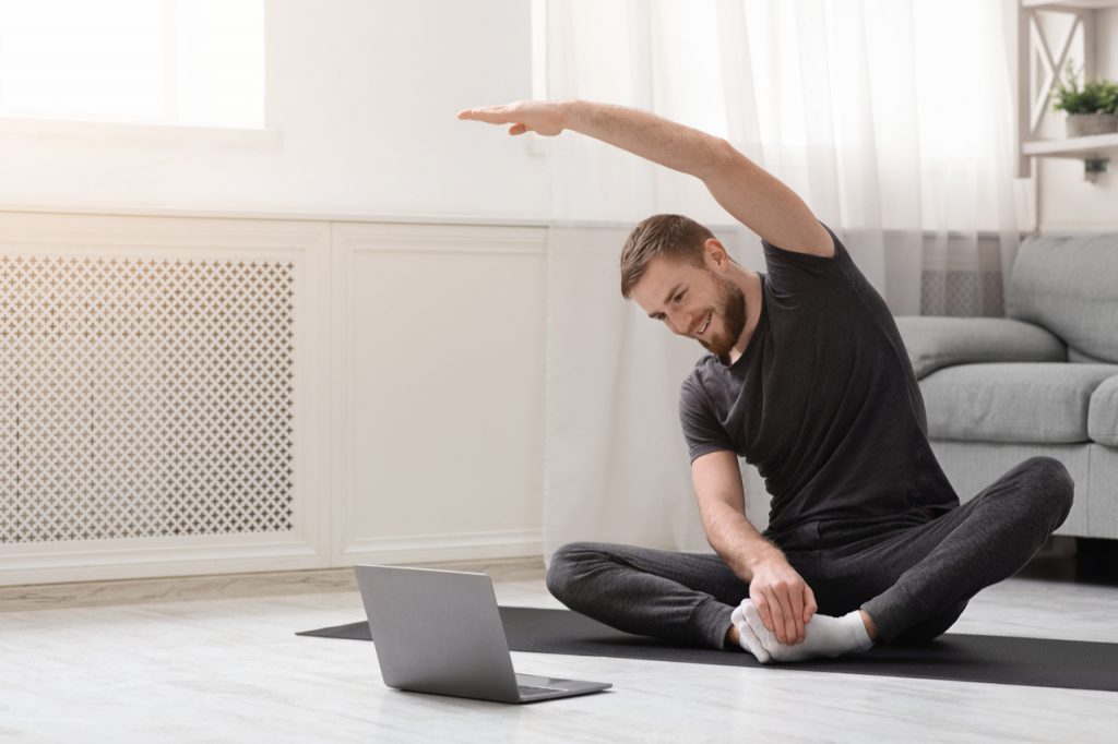 Man practicing yoga at home during an online fitness class.