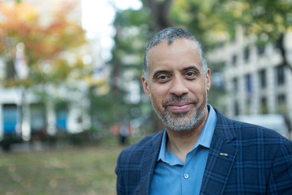 Larry Sharpe in the park wearing a checkered navy blue coat with blue shirt underneath.