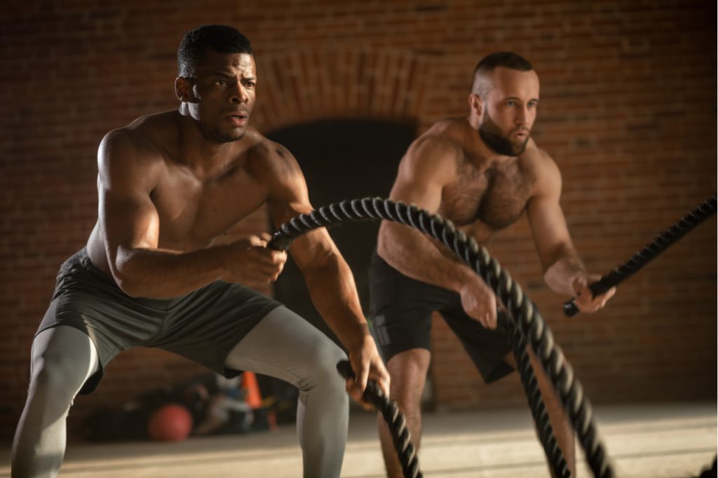 Two multiethnic atletic friends test the strength of an invisible enemy with battle rope in crossfit style.