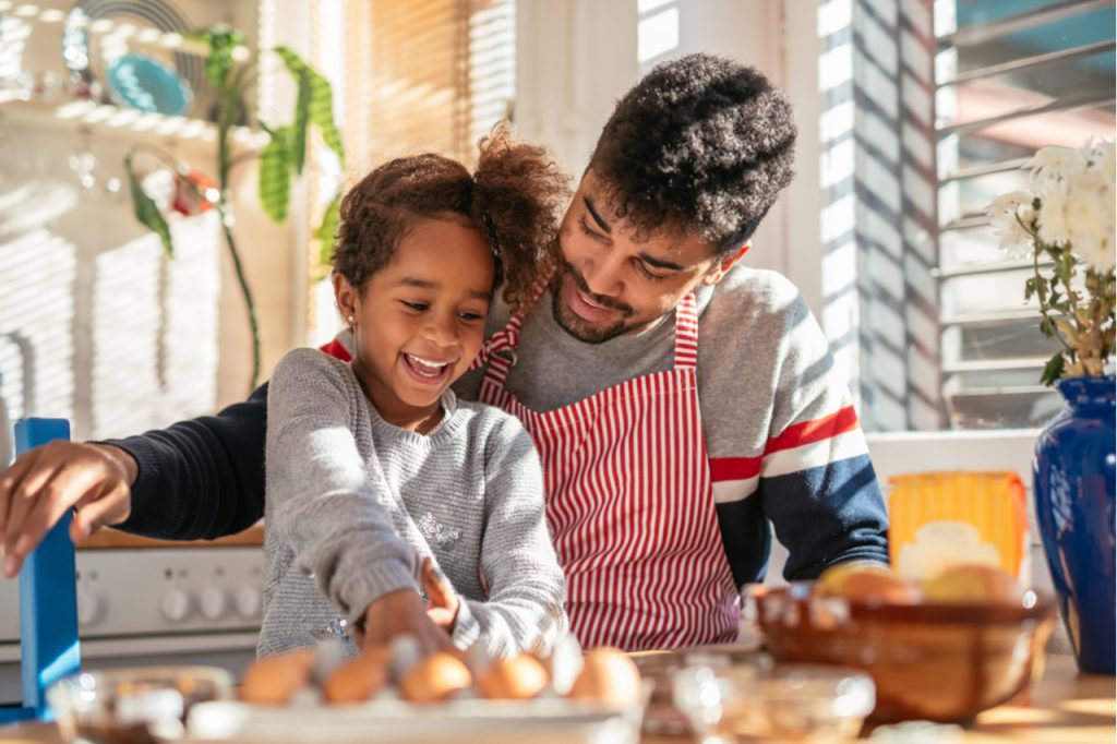 Photo of a smiling father and daughter baking in the kitchen and having fun.