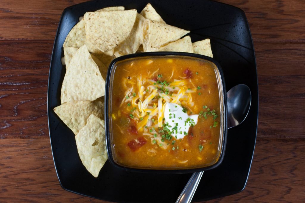 A bowl of chicken enchilada soup with a some tortilla on the side.