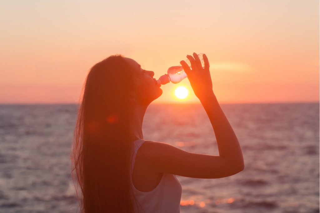 Woman drinking water by the sea.