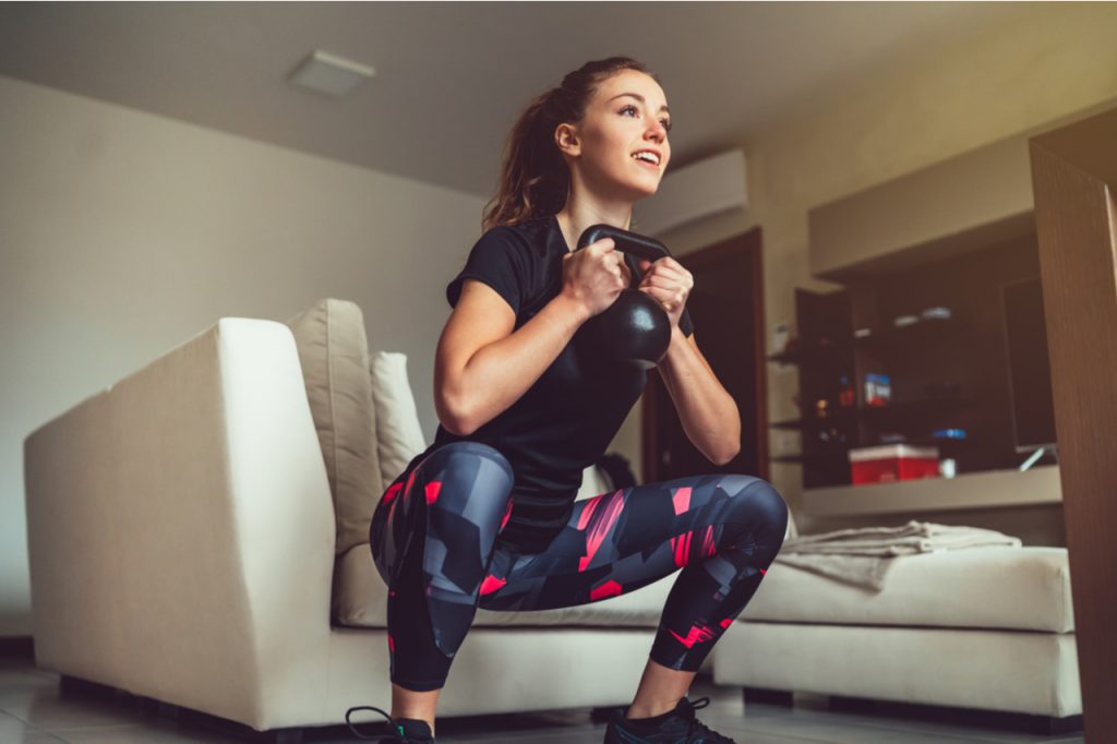 A woman working out in her living room holding a dumbbell fighting quarantine 15.