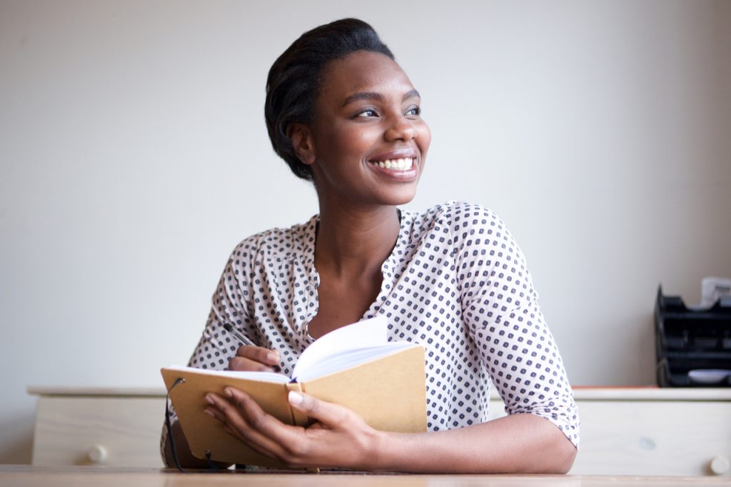 Portrait of smiling woman writing in journal at home.